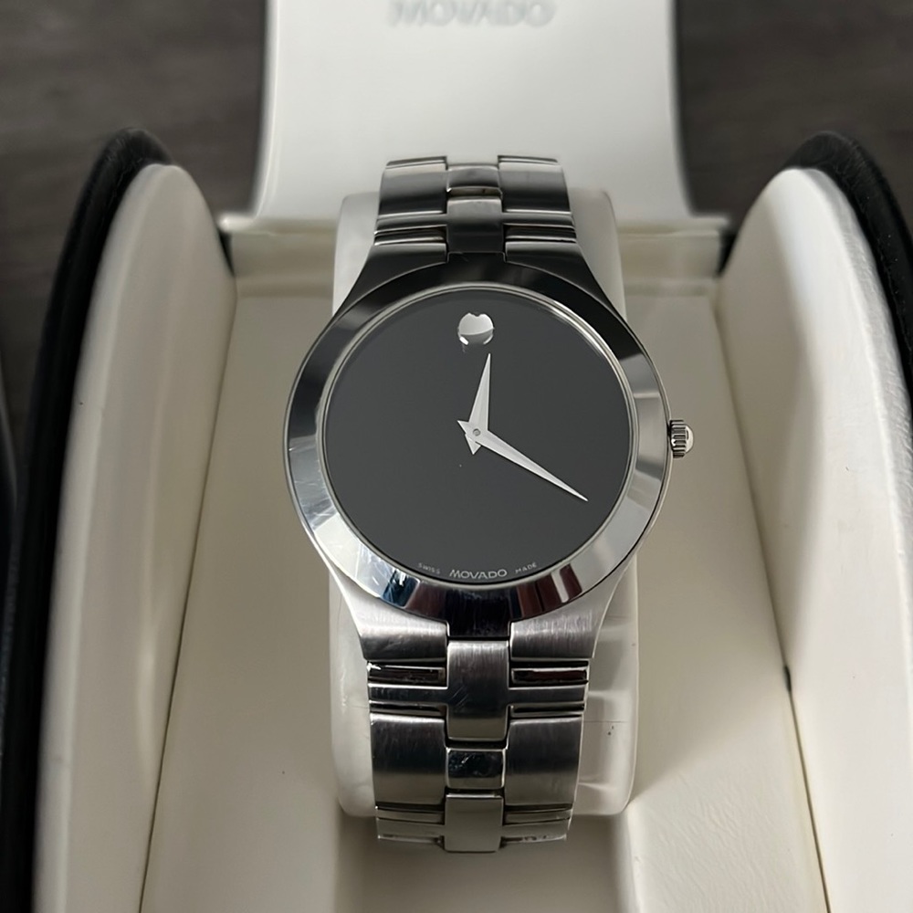 Men’s Preowned Movado quartz watch chrome finish black face. Comes in box